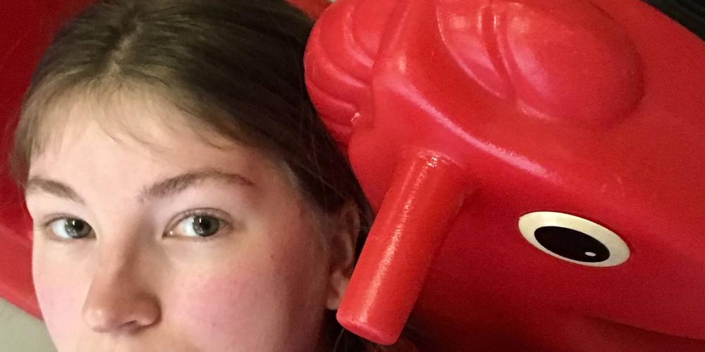 A close-up of someone lying against a red plastic rocking horse