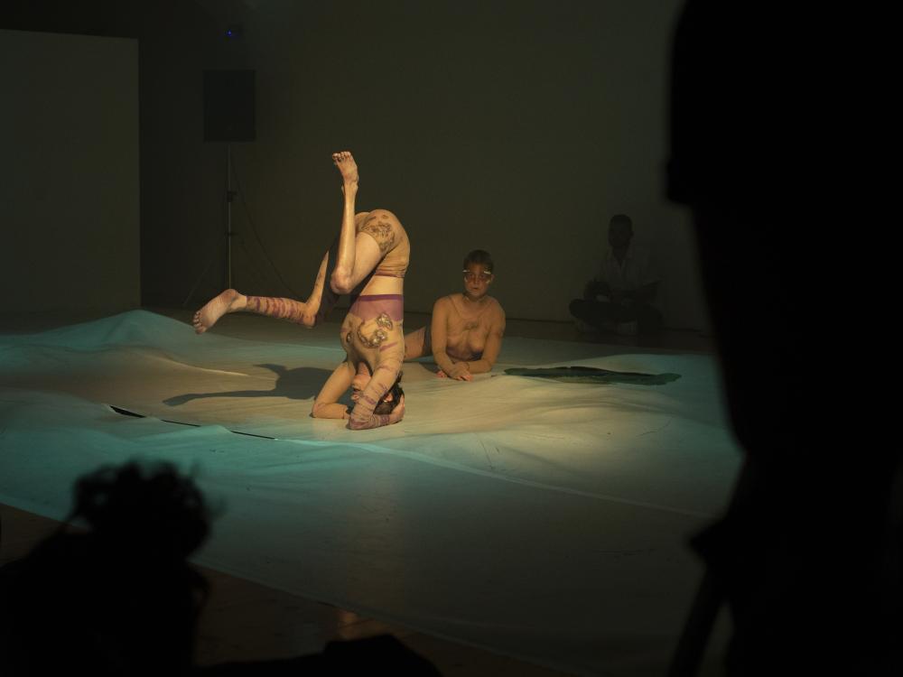 Two dancers on scene, one doing a headstand, the other lying on their stomach
