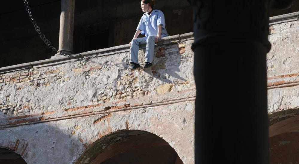 A young person sitting on the ledge of an old brick wall