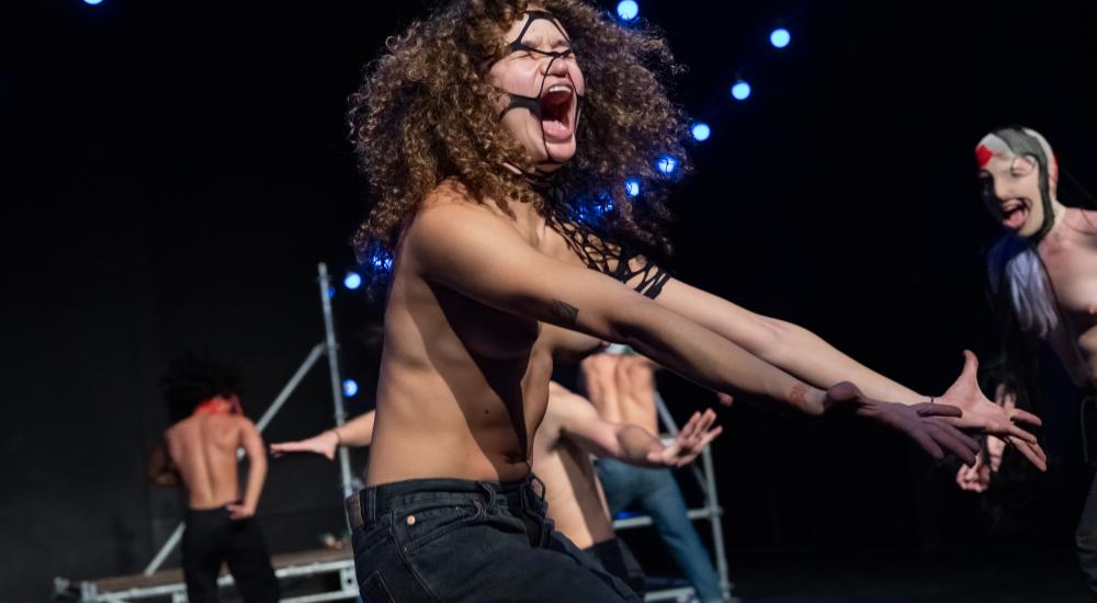 A dancer wearing jeans and no short screaming and thrusting their arms out in front of them