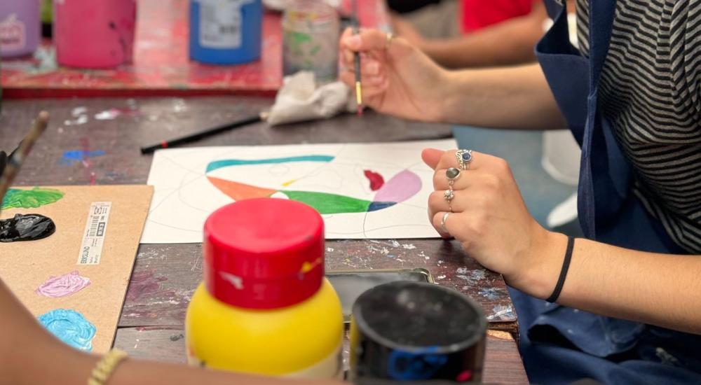 A person wearing an apron sitting at a table painting on a piece of paper