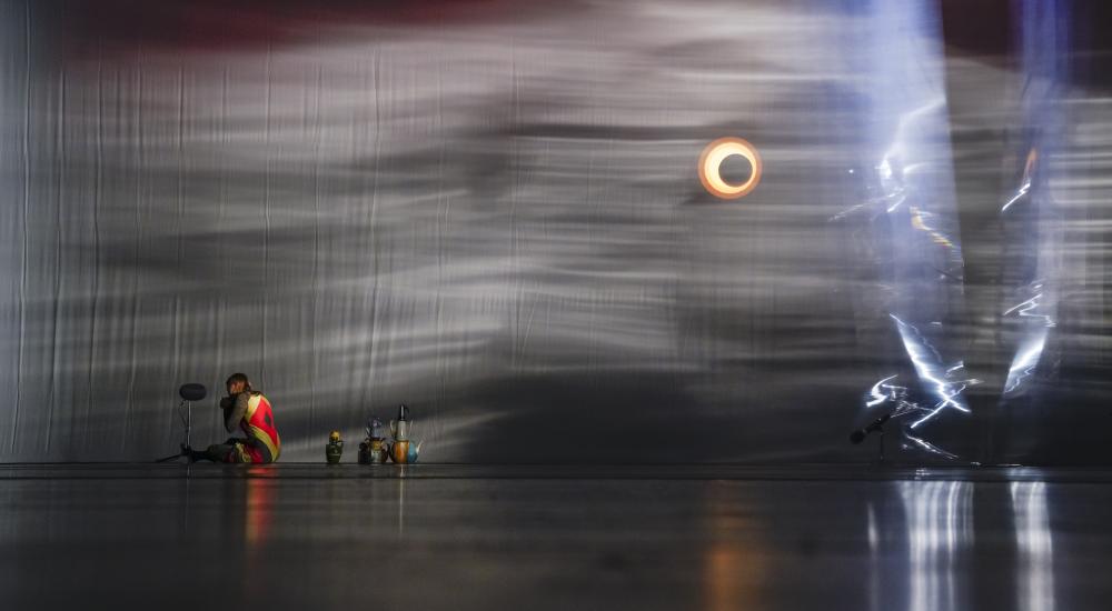 A person sitting on the floor at the back of the stage next to coloured teapots