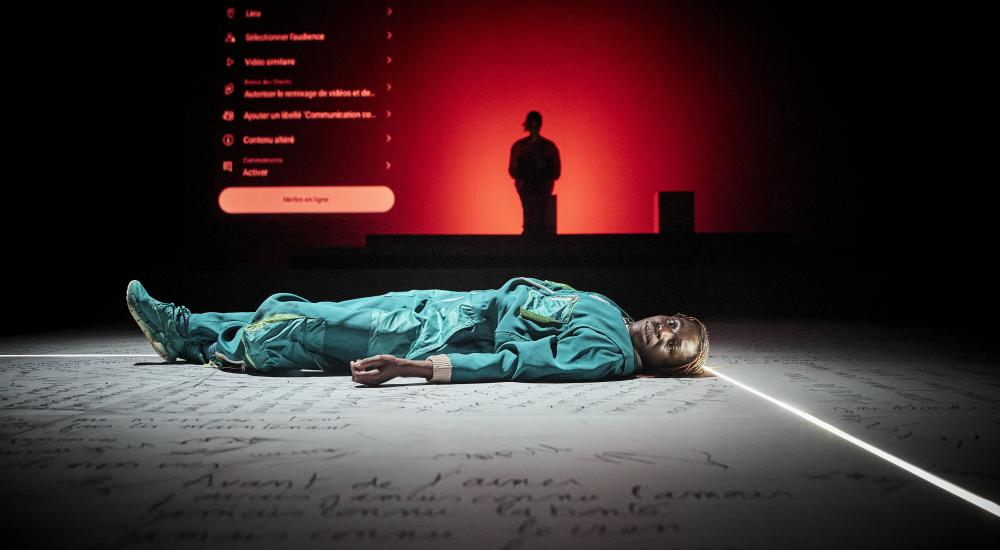 Dorothée lying on the floor, which is covered in text, with a person standing in the background surrounded by red lighting