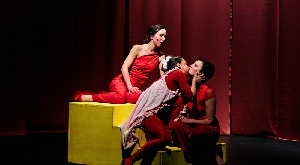 3 performers sitting on stairs two are kissing