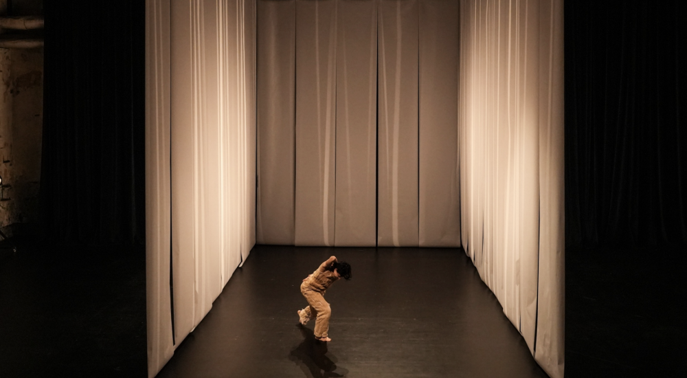 A person moving on a stage surrounded by white curtains on three sides