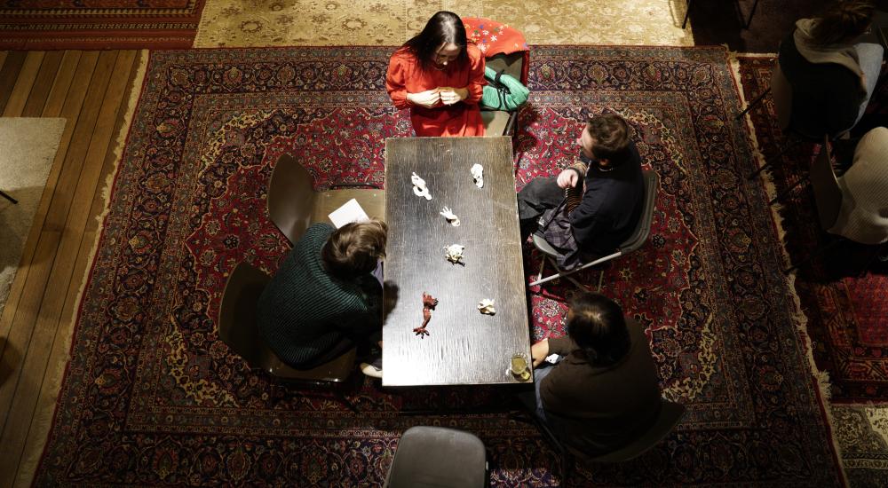 Bird's eye view of a table with four people sitting around it, on top of a Persian rug