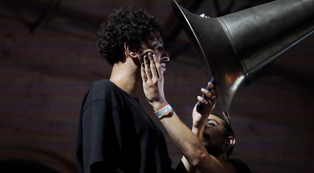 person standing under a huge horn reading its smartphone while another person standing right of him is holding his face with one hand
