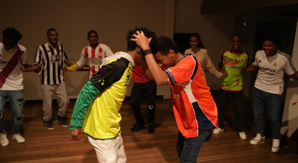 A group of people dancing in a circle with two people in the middle, heads against each other