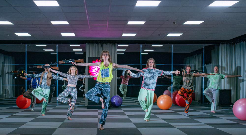 A group of people wearing colourful clothes in a yoga studio with exercise balls. Some of them are holding machine guns
