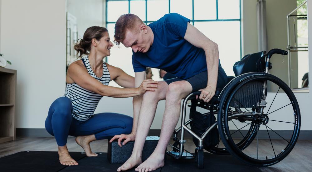 persoon in fysiotherapie in een rolstoel terwijl een therapeut de knie aanraakt