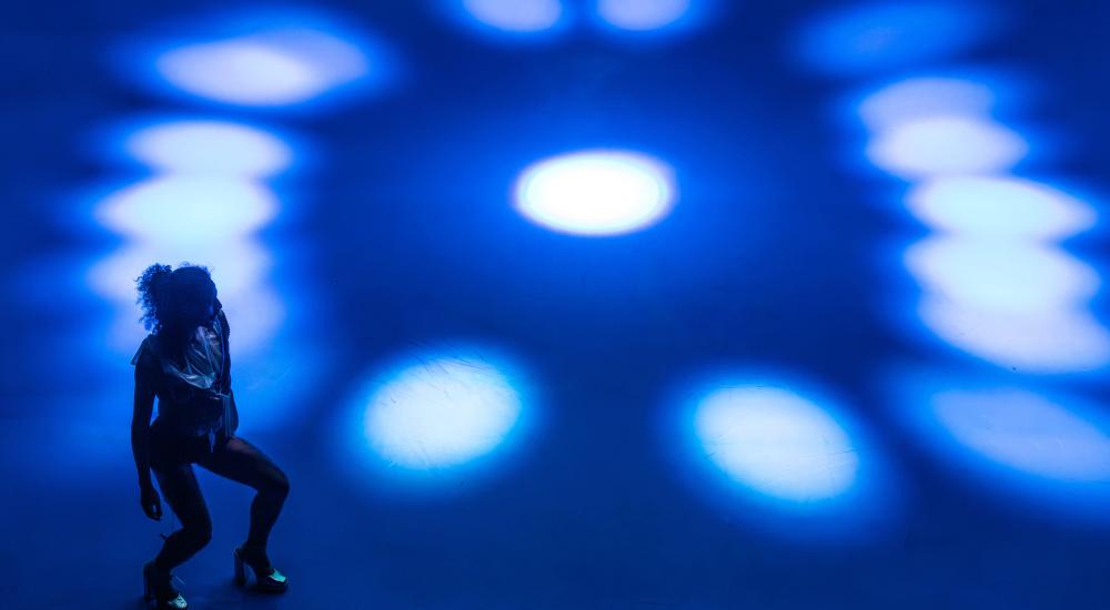 1 performer with black clothes dancing on a bright blue floor