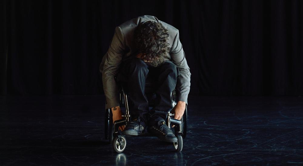 A person on a wheelchair with their body folded forward and their hands hanging downwards