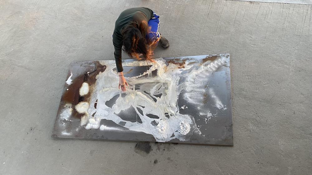 A person putting white paint on a sheet of metal