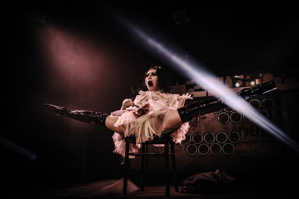 Majo wearing a white frilly dress and high black boots lying on a chair with their legs open