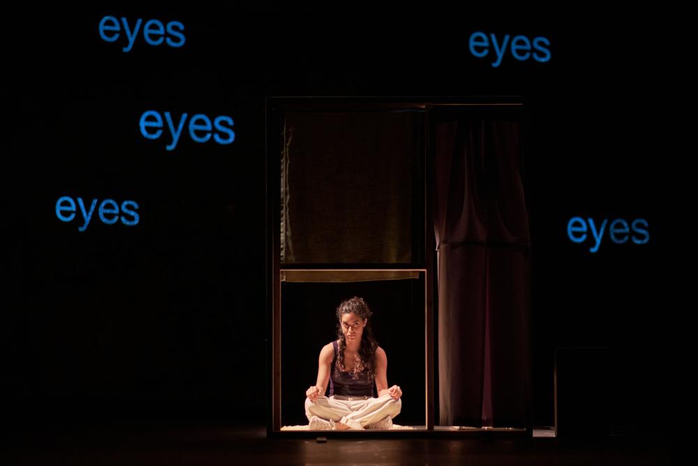 Marah sitting crosslegged in front of the word 'eyes' projected five times on the wall