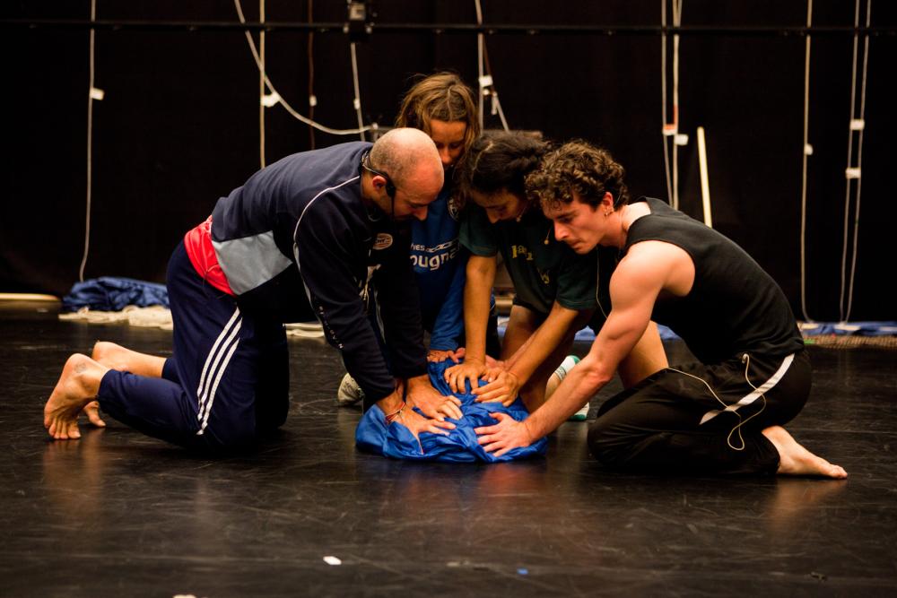 Three performers pressing down on a blue sheet