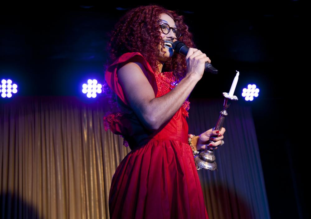 A drag artist with red hair wearing a red dress holding a microphone