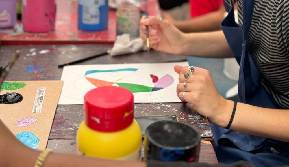 A person wearing an apron sitting at a table painting on a piece of paper