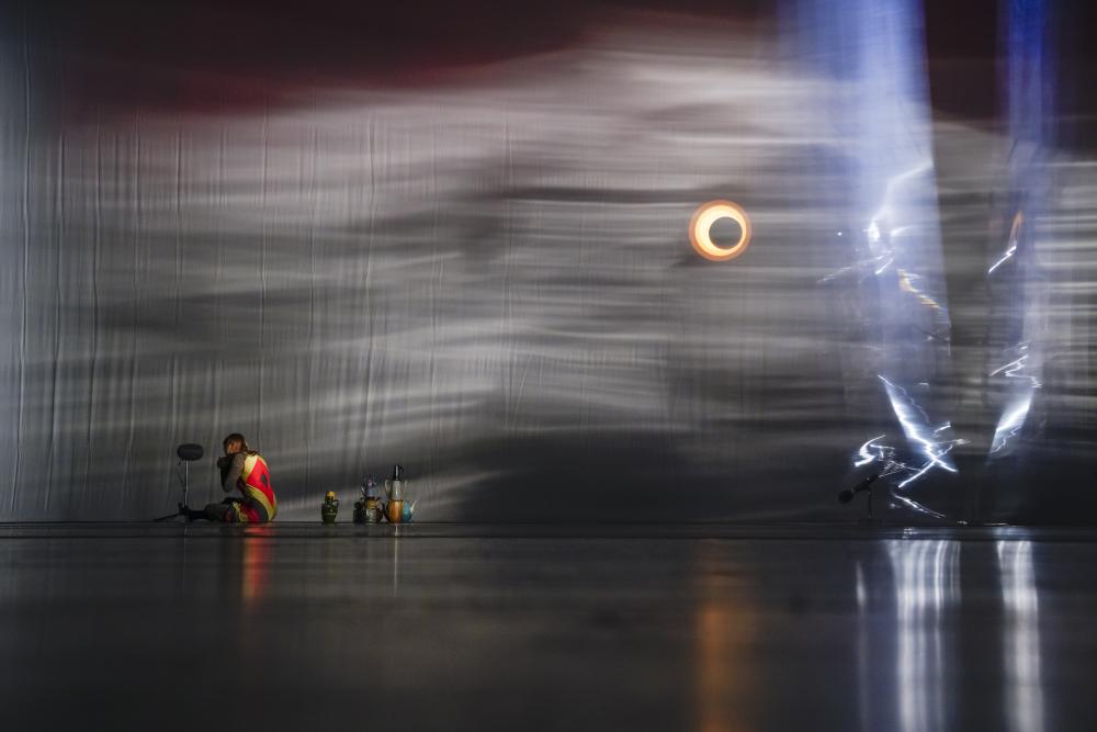 A person sitting on the floor at the back of the stage next to coloured teapots