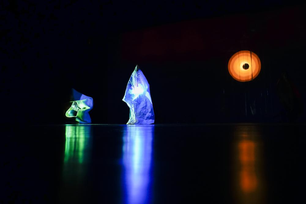 Two people in cloaks holding a green and blue light respectively that shine through their cloaks