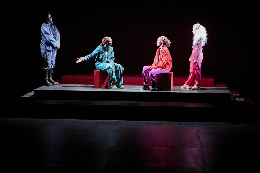 Four people on stage, two standing, two on stools