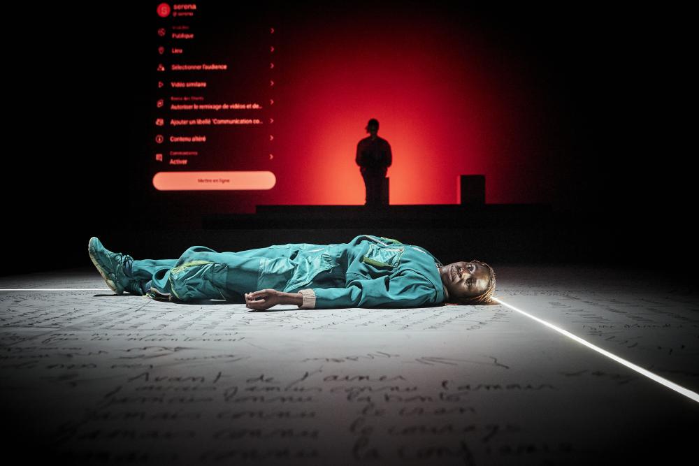 Dorothée lying on the floor, which is covered in text, with a person standing in the background surrounded by red lighting