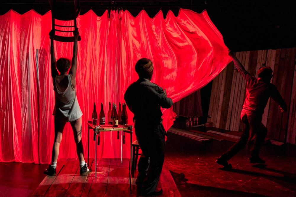 Michiel pulling a curtain lit up by red light and Aurélie holding a chair over her head