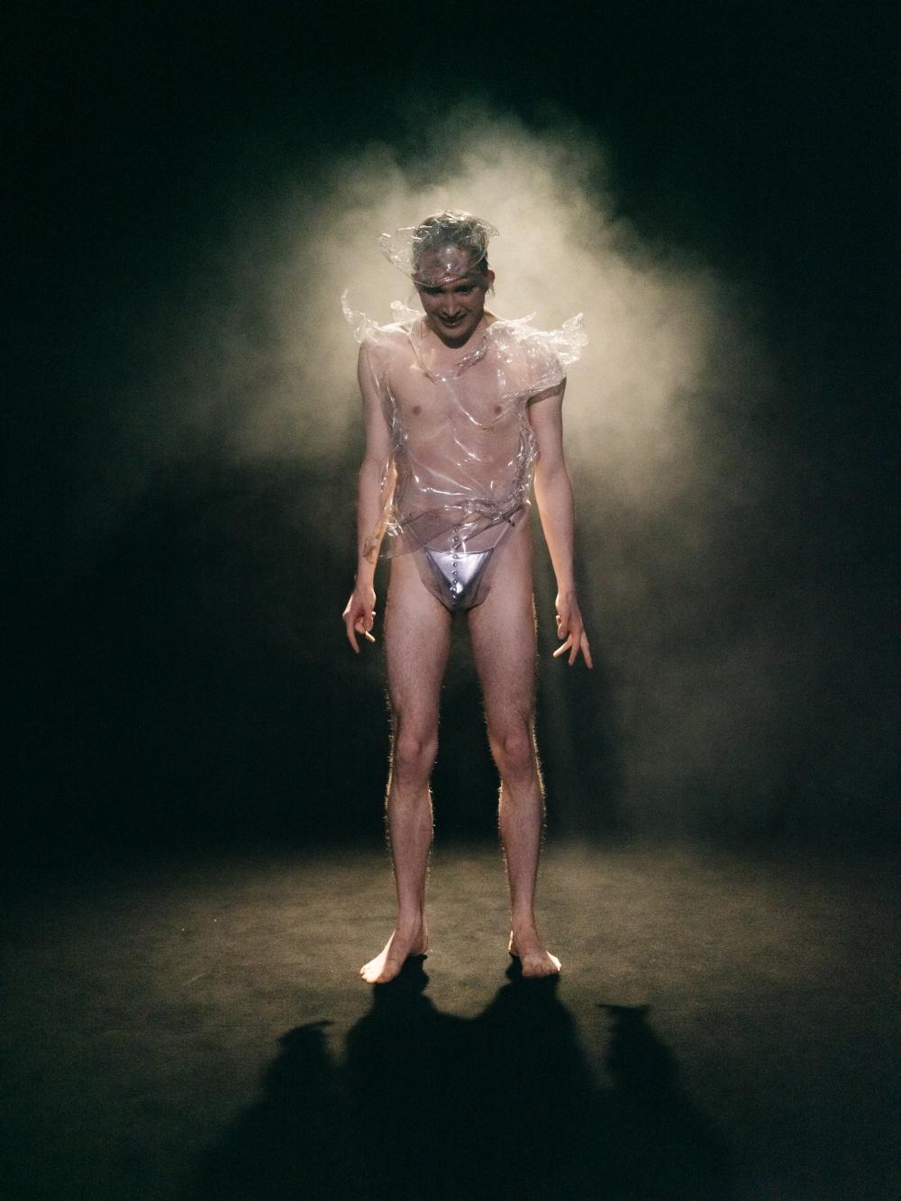 image of a performer only wearing underwear standing on the stage with a spotlight and smoke in the back