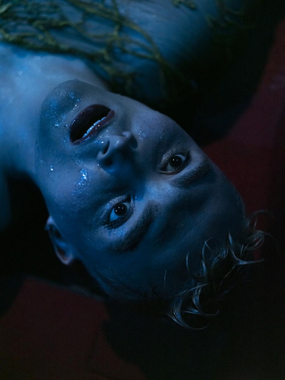 close up of a performer laying on the floor with a blue light on its face