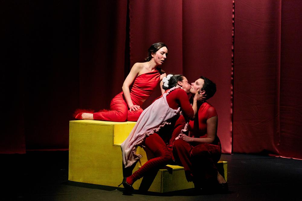 3 performers sitting on stairs two are kissing