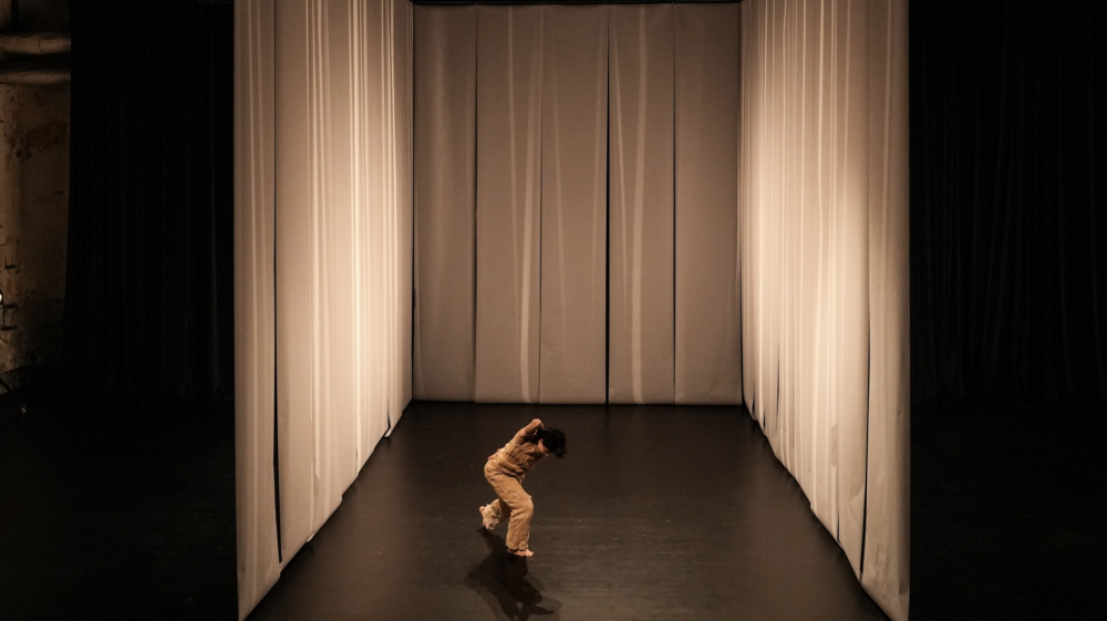 A person moving on a stage surrounded by white curtains on three sides