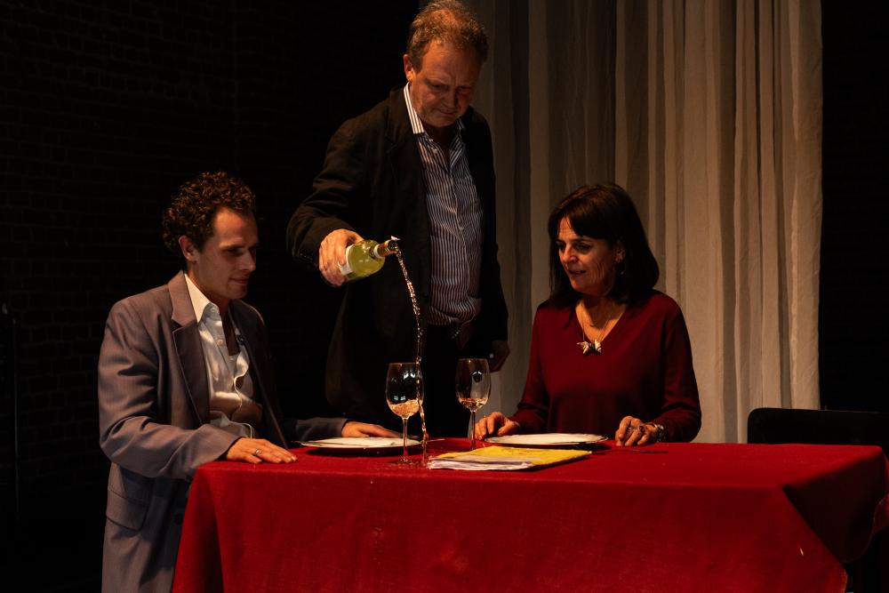 Frank and his mother sitting at a table being served by a waiter pouring wine on the table