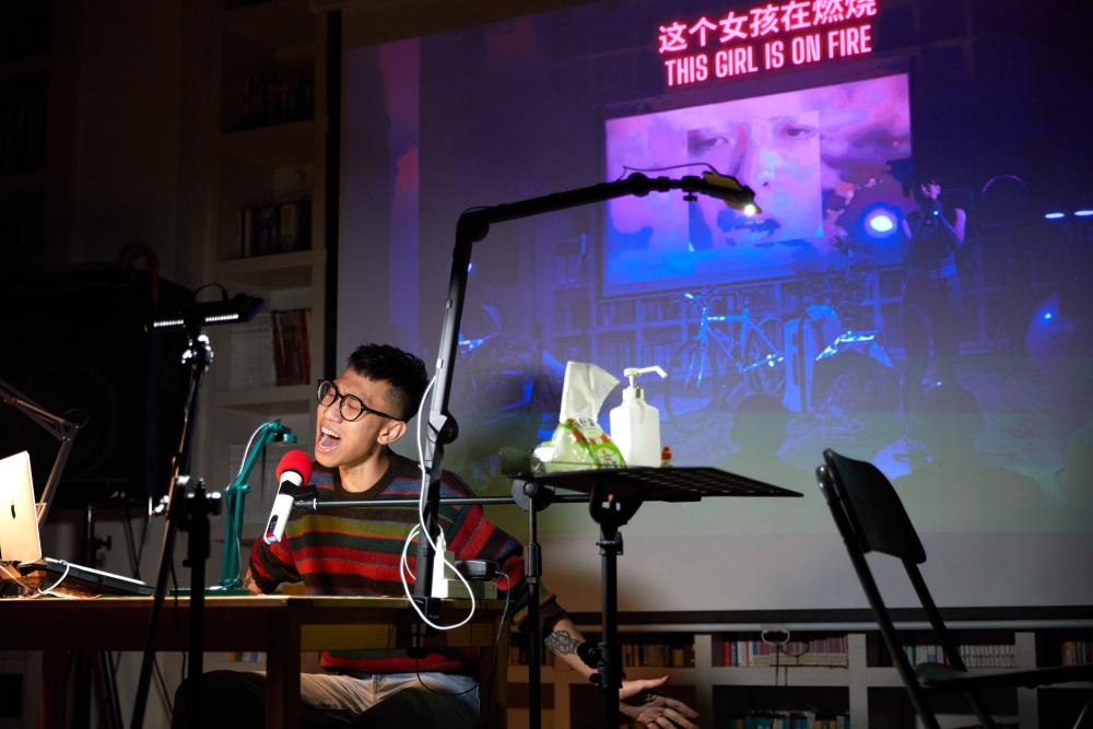 Ping-Hsiang sitting behind a desk singing in front of a screen which reads "This Girl is on Fire"