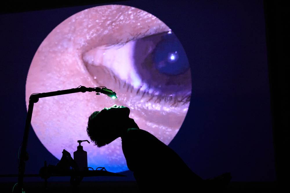 Ping-Hsiang leaning back under a camera which is projecting his eye on the wall behind him