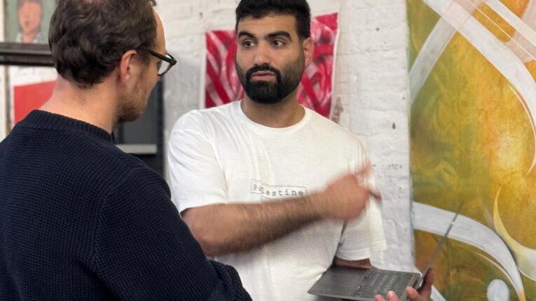 A man holding a laptop pointing towards a painting