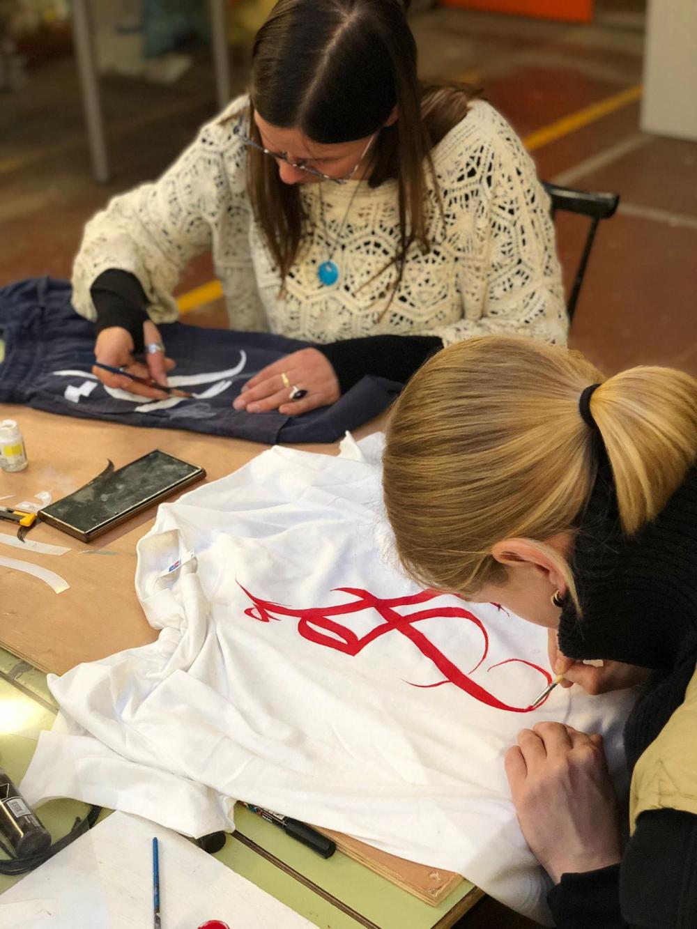 Two people painting Arabic letters on T-shirts