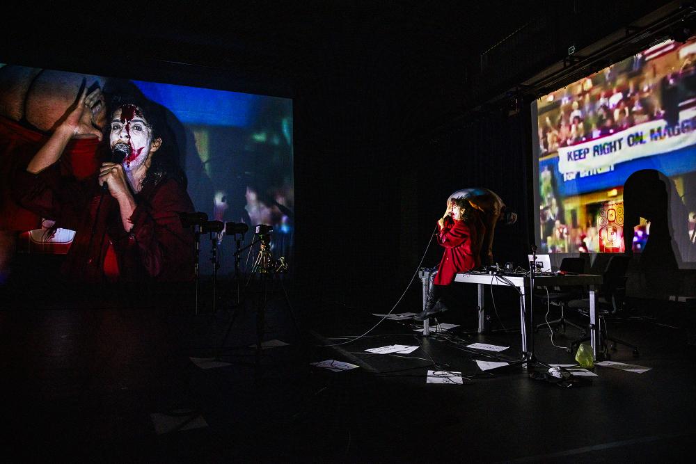 Rodrigo and Mariana in Joker-style clown's makeup surrounded by projections