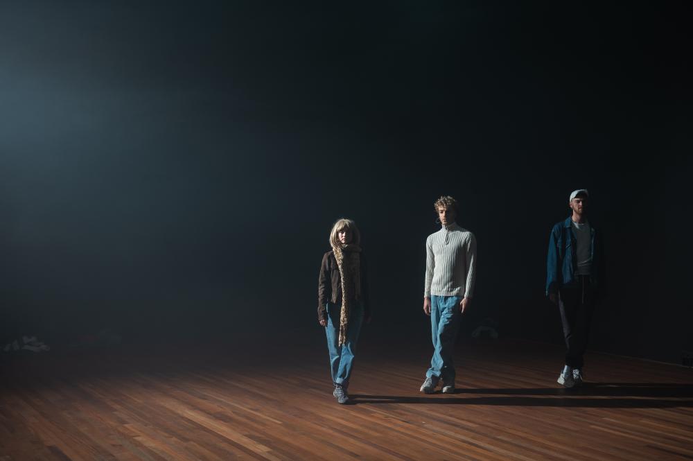 Three performers standing on a hardwood floor
