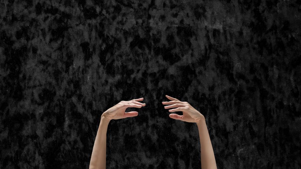 Two hands in a ballet pose in front of a black background