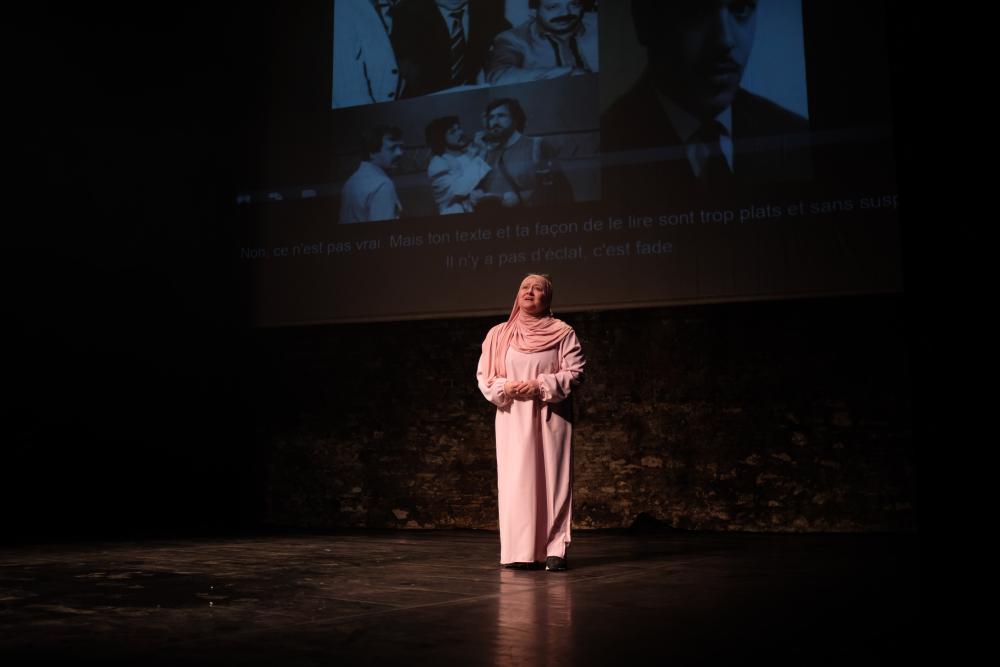 A person on stage wearing a long white dress in front of a projection of a family photo