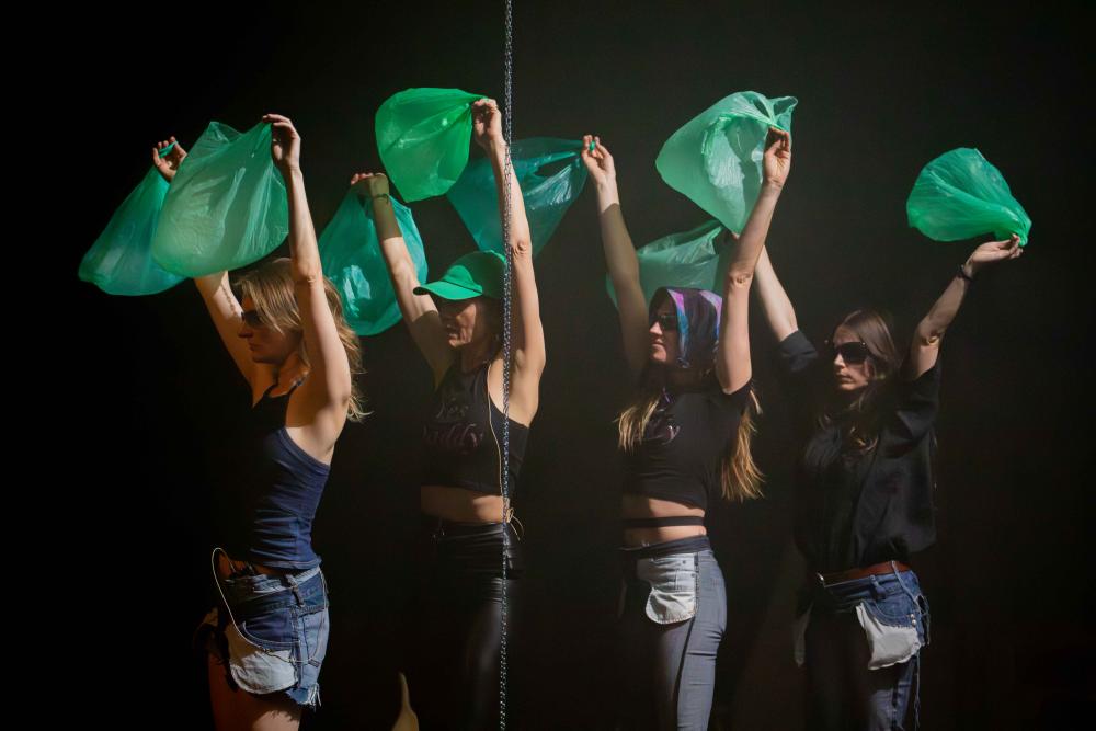 Four women in sunglasses holding green bin bags above their heads