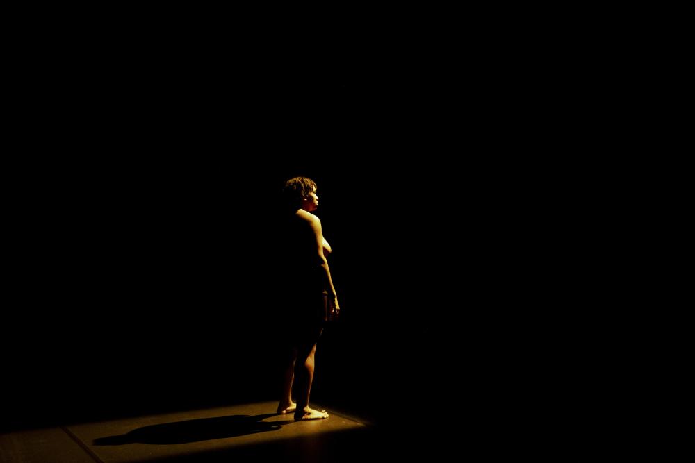 Black halfnaked person on stage in yellow spotlight