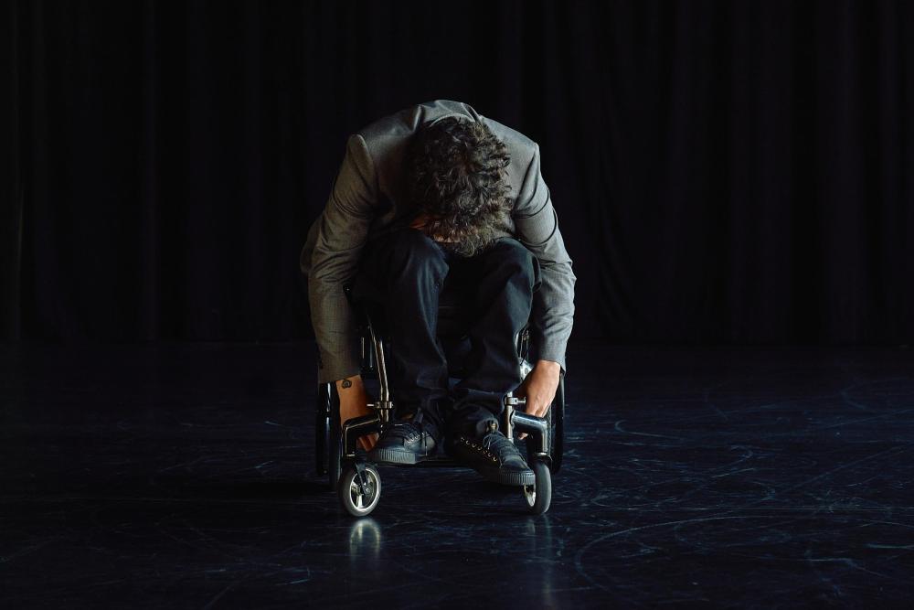 A person on a wheelchair with their body folded forward and their hands hanging downwards