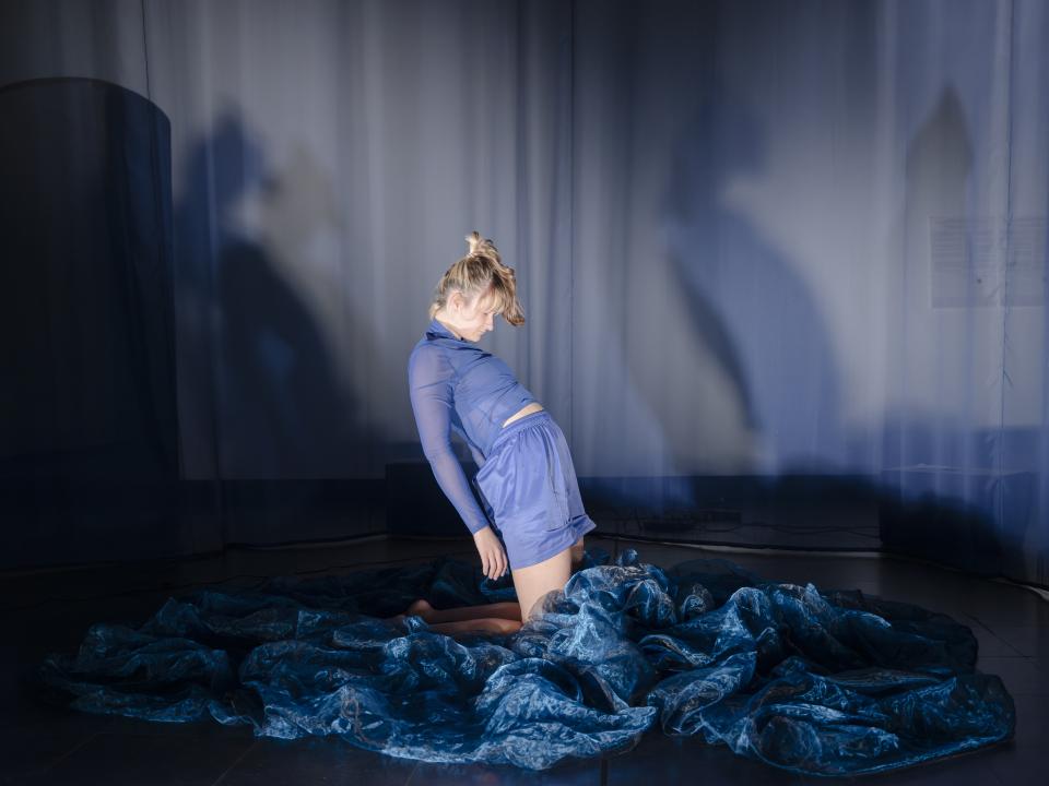 Anna sitting on her knees, leaning back on a table covered in a flowy blue cloth
