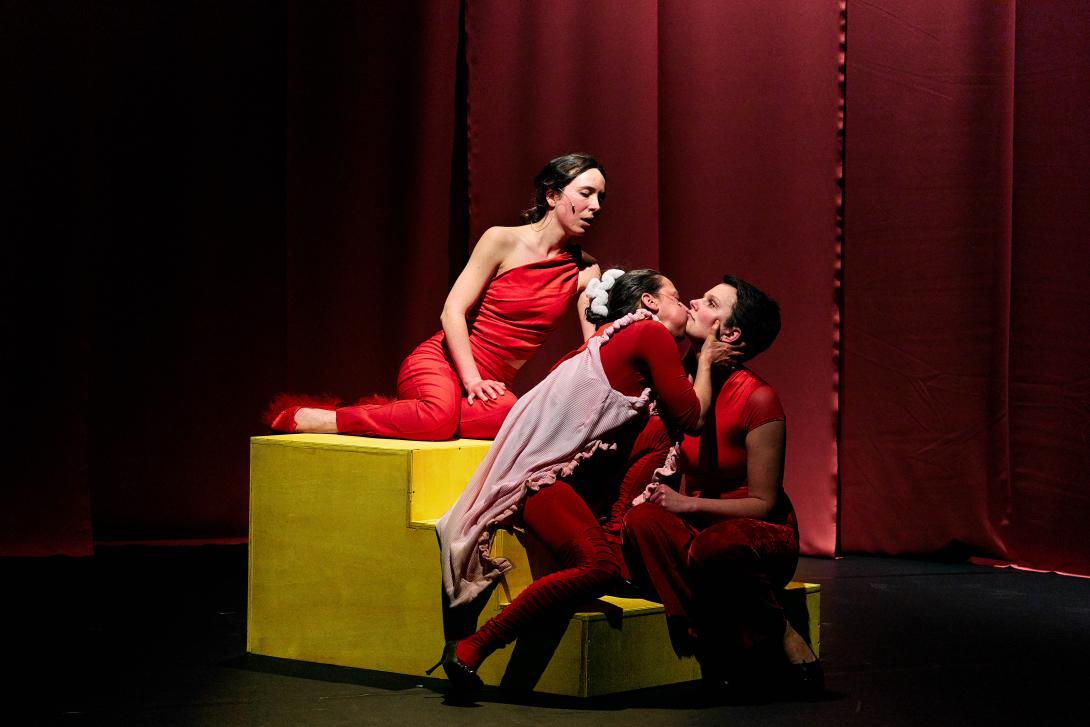 3 performers sitting on stairs two are kissing