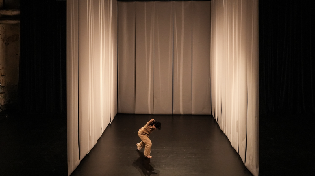 A person moving on a stage surrounded by white curtains on three sides