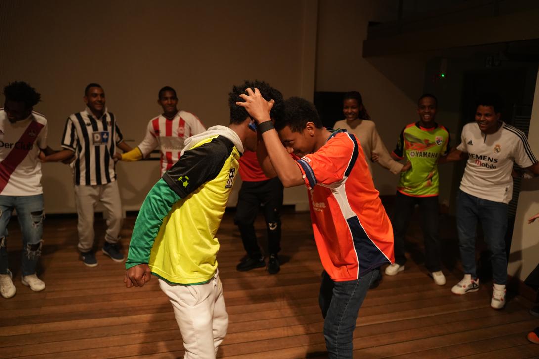 A group of people dancing in a circle with two people in the middle, heads against each other