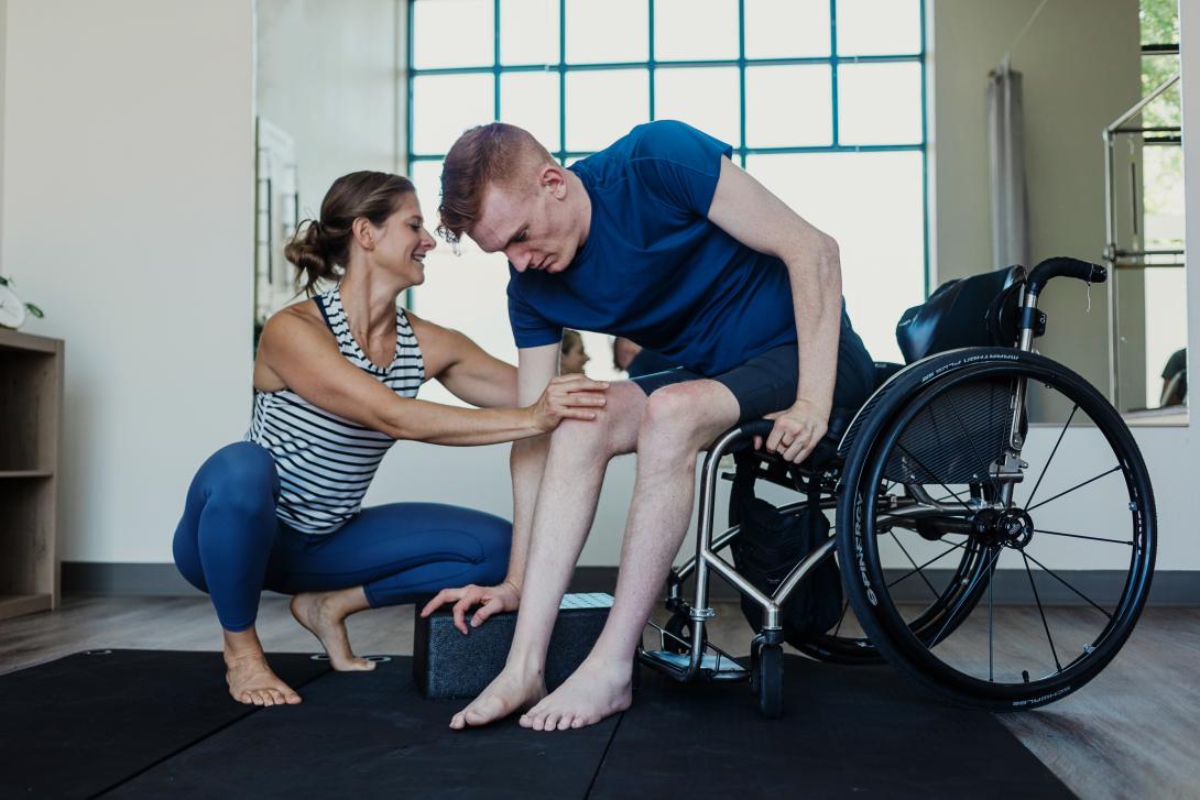 persoon in fysiotherapie in een rolstoel terwijl een therapeut de knie aanraakt